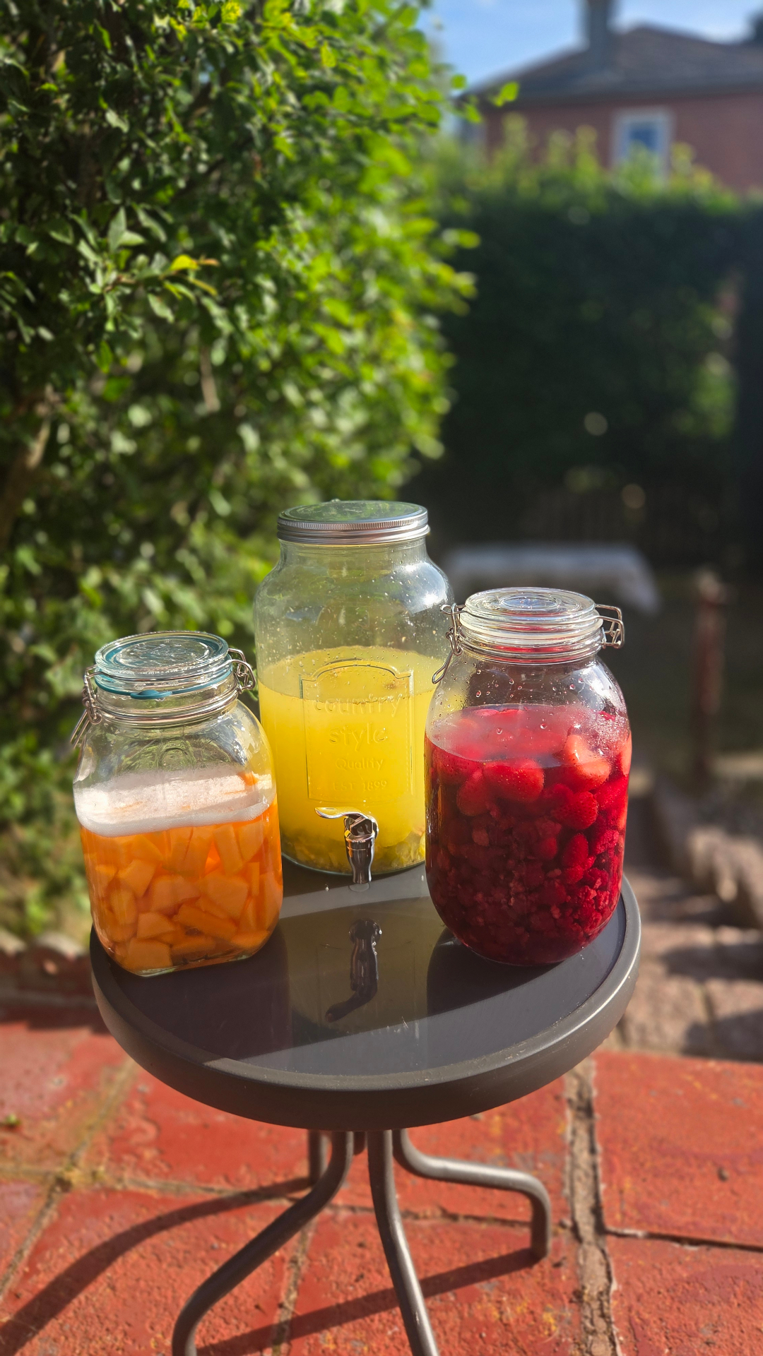 Bocaux de fruits en infusion posés sur une table de jardin, au soleil